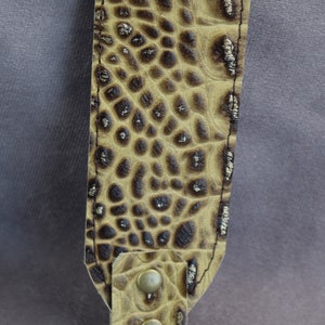 Peut inclure: Un porte-clés en cuir marron avec un motif crocodile et un fermoir en métal doré.