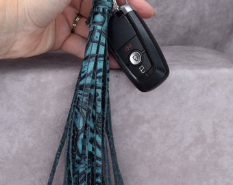 May include: A teal blue leather tassel keychain with a black and white pattern. The keychain is attached to a silver key ring and a black car key fob.