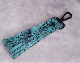 May include: A teal blue leather tassel keychain with a black metal clip. The tassel has a paisley pattern.