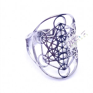 May include: A silver ring with a geometric design. The design is a complex pattern of lines and circles, resembling a flower or a star.