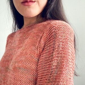 K&ouml;nnte beinhalten: Nahaufnahme eines gestrickten Pullovers in hellpfirsichfarben. Der Pullover hat einen Boot Ausschnitt und lange &Auml;rmel.
