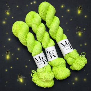 May include: Three skeins of neon yellow yarn with subtle blue speckles, each wrapped in a white paper label featuring the black text MK MOLLYKLEINDESIGN EST. 2015. The yarn is arranged diagonally against a dark background with glowing fireflies.