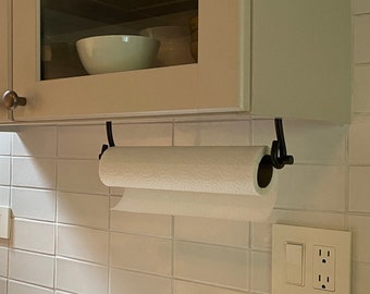 May include: White kitchen cabinets with glass doors above a white tiled backsplash. A paper towel holder is mounted under the cabinets with a roll of paper towels. A white countertop is below the backsplash.