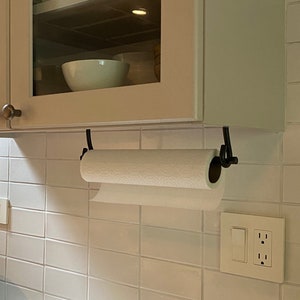 May include: White kitchen cabinets with glass doors above a white tiled backsplash. A paper towel holder is mounted under the cabinets with a roll of paper towels. A white countertop is below the backsplash.