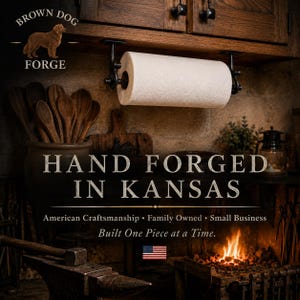 Może przedstawiać: Czarny metalowy uchwyt na ręcznik papierowy zamontowany pod drewnianą szafką. Obraz zawiera tekst BROWN DOG FORGE, HAND FORGED IN KANSAS, American Craftsmanship, Family Owned, Small Business, Built One Piece at a Time oraz flagę USA.
