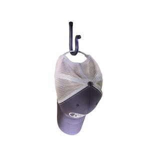 May include: A black metal hook with a curved design, holding a gray and white baseball cap with a logo on the front.