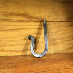May include: A black metal hook with a hammered finish. The hook is shaped like a 'J' and has a rounded top.