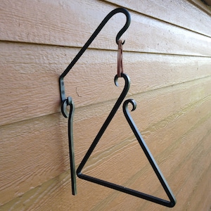 May include: A black metal triangle chime with a hanging striker. The chime is mounted on a wall with a black metal bracket.