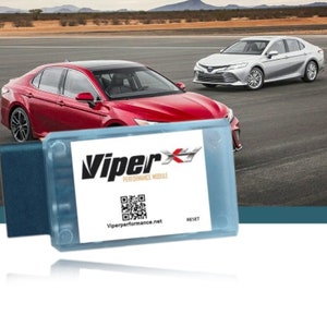 May include: A blue and white Viper Performance Module with a QR code and the text "Viper Performance Module" and "Viperperformance.net". The module has a reset button. The module is in front of two silver cars on a race track.