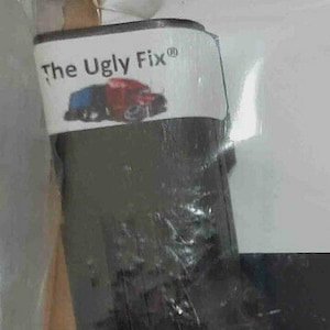 May include: A product package with the text "The Ugly Fix®" in white on a white label. The label features a graphic of a blue and red truck. The package is dark gray and partially obscured by clear plastic.
