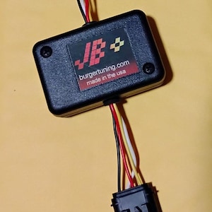 May include: A black rectangular electronic tuning module with a label reading JB+ burgertuning.com made in the usa. The device features two sets of multi-colored wires, including black, white, red, and yellow, connected to two black plastic connectors.