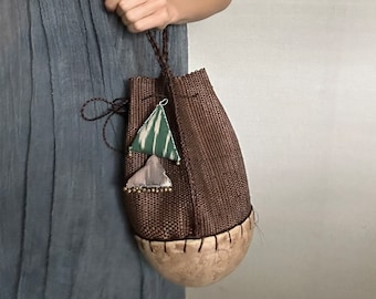 May include: A brown woven bag with a drawstring closure and a decorative tassel. The bag is made from natural materials and has a unique, rustic look.