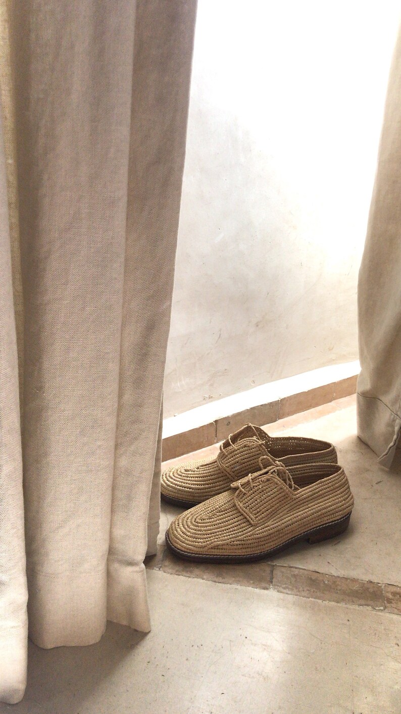 K&ouml;nnte beinhalten: Ein Paar geflochtene Strohschuhe mit Schn&uuml;rsenkeln. Die Schuhe sind hellbraun und haben eine leicht spitz zulaufende Spitze. Die Schuhe stehen auf einem hellbraunen Fliesenboden.