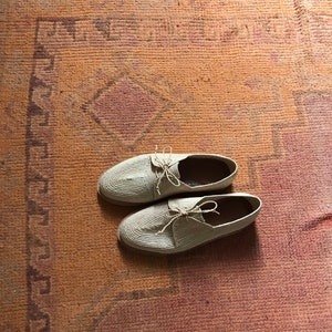 K&ouml;nnte beinhalten: Zwei Paar beige geh&auml;kelte Schuhe mit Schn&uuml;rsenkeln auf einem gemusterten Teppich.
