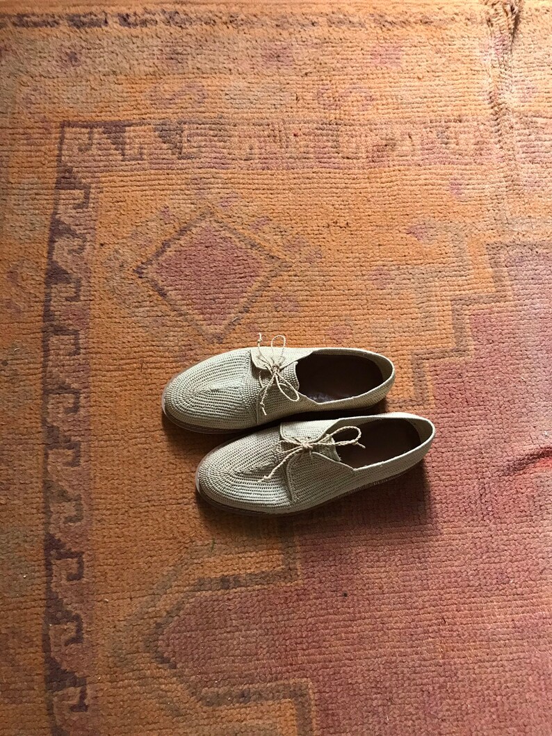 K&ouml;nnte beinhalten: Zwei Paar beige geh&auml;kelte Schuhe mit Schn&uuml;rsenkeln auf einem gemusterten Teppich.