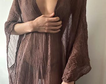 Puede incluir: Un vestido largo, holgado, de manga larga y transparente, de color marrón, con un escote en V profundo.