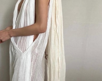 May include: A white sheer sleeveless dress with a long white scarf draped around the neck and shoulders.