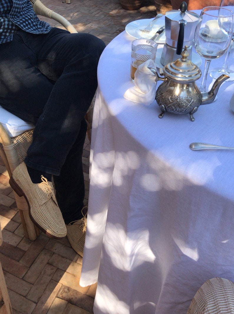 K&ouml;nnte beinhalten: Eine wei&szlig;e Tischdecke mit einer silbernen Teekanne, einem Glas Tee und einem silbernen L&ouml;ffel. Eine Person in blauen Jeans und braunen Schuhen sitzt an einem Tisch mit einer wei&szlig;en Tischdecke.