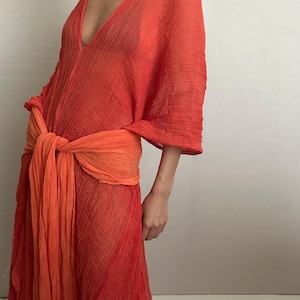 May include: A long, flowing, orange and red sheer dress with a deep V-neck and a tie at the waist.