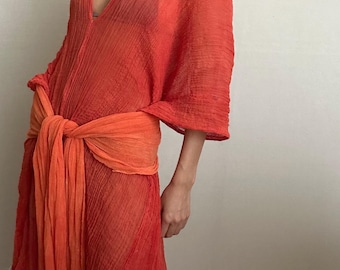 May include: A long, flowing, orange and red sheer dress with a deep V-neck and a tie at the waist.