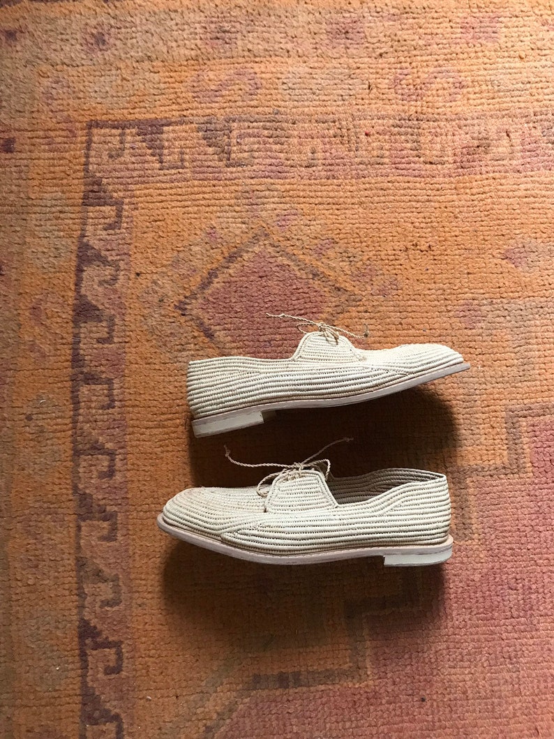 K&ouml;nnte beinhalten: Zwei Paar wei&szlig;e gewebte Schuhe mit Schn&uuml;rsenkeln auf einem braunen gemusterten Teppich.