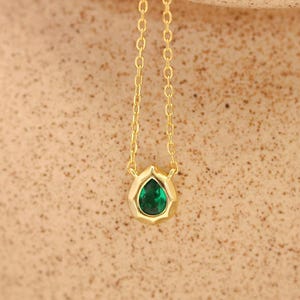 May include: A delicate gold necklace with a teardrop-shaped, emerald-green gemstone pendant. The pendant is set in a gold bezel and hangs from a fine gold chain. The necklace is displayed against a neutral background.