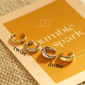 May include: Four ear cuffs in gold and silver tones are displayed on a mustard-colored card with the words "humble spark". The ear cuffs include a twisted design, a dome shape, and other styles.