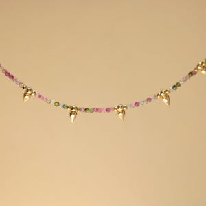 May include: A delicate necklace featuring a strand of small, colorful beads in shades of pink, green, and white. Gold-colored, pointed accents are evenly spaced along the necklace, creating a unique and elegant design.