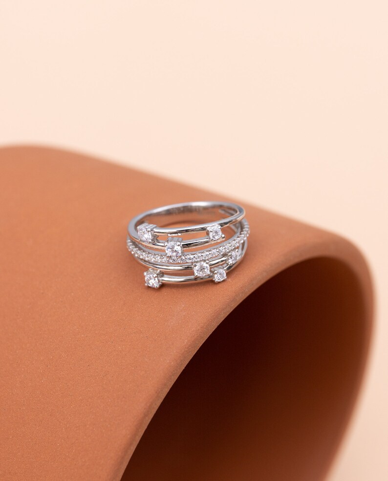 May include: A silver ring with multiple bands and small clear stones. The ring is on a brown surface.