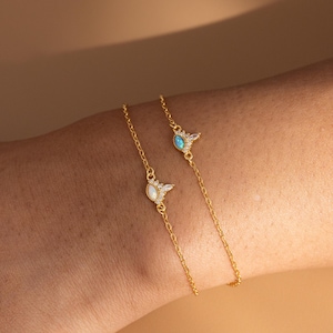 以下が含まれることがあります： 繊細なデザインのゴールドチェーンブレスレット2本。1本は、小さな石のハローが付いた白いオパールストーン、もう1本は、小さな石のハローが付いた青いオパールストーンが特徴です。