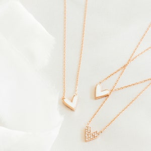 May include: Three gold necklaces with heart pendants. Two of the pendants are white enamel and one is encrusted with small clear stones.