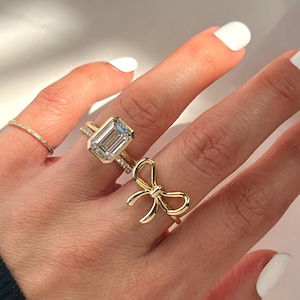 May include: A gold ring with a large emerald-cut diamond and a smaller gold ring with a bow design.
