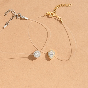 May include: Two delicate necklaces with clear, nearly invisible cords. One features a round, silver-toned pendant with a halo of small, clear stones. The other has a gold-toned chain and a pear-shaped pendant with clear stones. Both have adjustable clasps.