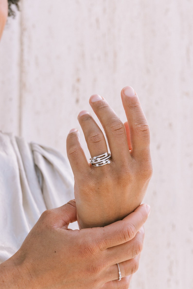 May include: A person wearing a stack of five silver rings with small clear stones on each ring.