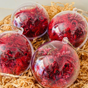 May include: Four clear glass baubles filled with red dried flowers and greenery. The baubles are sitting in a brown shredded paper basket.