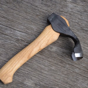 Pode incluir: Uma ferramenta de escultura com cabo de madeira e uma lâmina preta curva. A lâmina é afiada na borda interna e tem uma pequena área plana na borda externa.