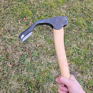 May include: A black and brown woodworking tool with a wooden handle. The tool is a curved adze with a sharp blade.