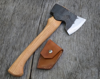 May include: A small, hand-forged axe with a wooden handle and a leather sheath. The axe has a black finish and a polished blade.