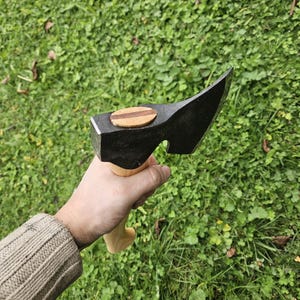 May include: A black hand axe with a wooden handle. The axe head has a small wooden inlay on the top.