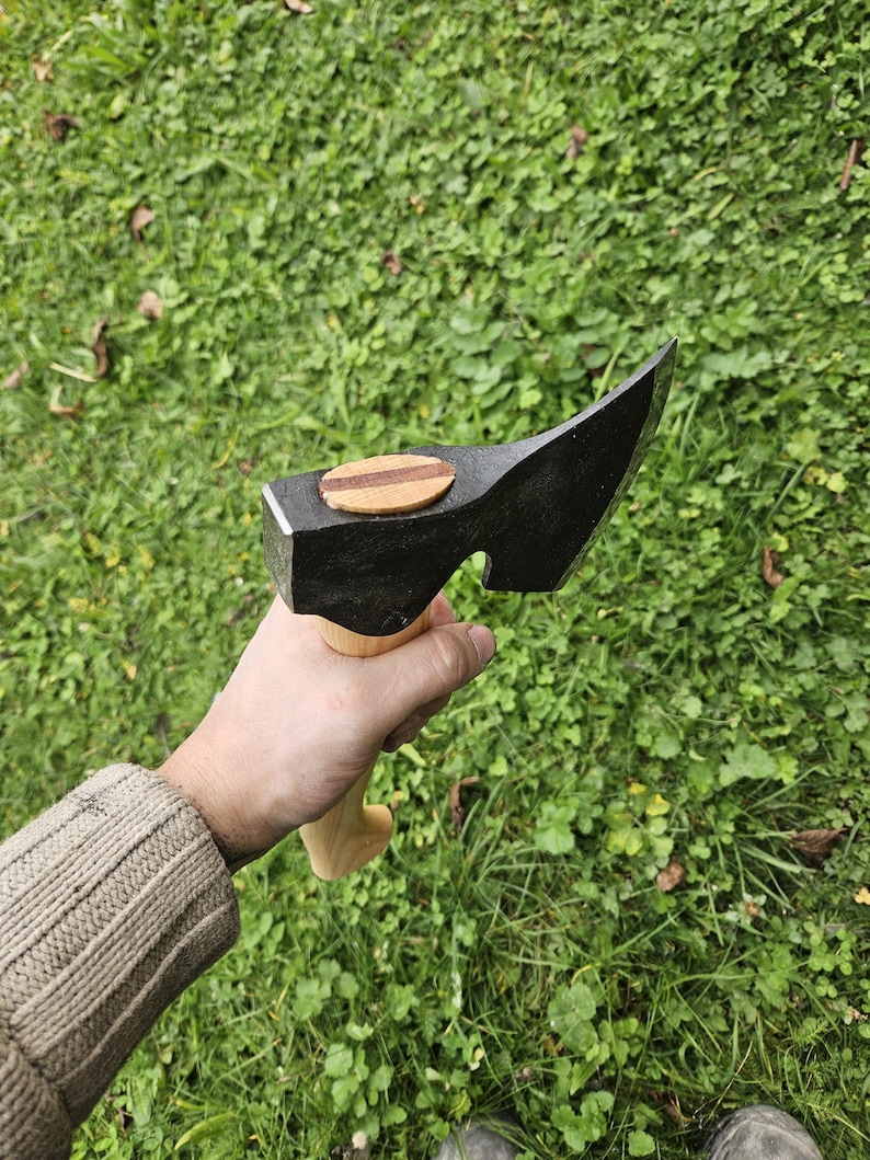 May include: A black hand axe with a wooden handle. The axe head has a small wooden inlay on the top.