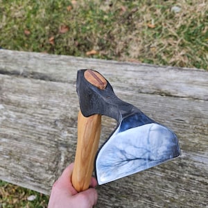 以下が含まれることがあります： 木製の柄が付いた、手打ちのカーブした刃の斧。斧は磨かれた反射する刃と、濃い茶色の仕上げの柄を持っている。