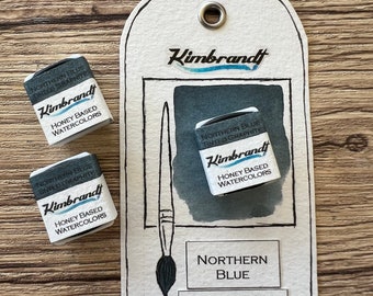 May include: Watercolor paint set featuring two individual paint cubes and a display card. The card includes a watercolor brush illustration and the text "Northern Blue, Tinted Graphite." The paint cubes and card display the "Kimbrandt" logo and "Honey Based Watercolors."