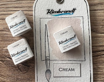 May include: A watercolor art set featuring three small cream-colored paint cubes and a tag with the brand name "Kimbrandt." The tag includes a watercolor brush illustration and the word "CREAM." The set is honey-based.