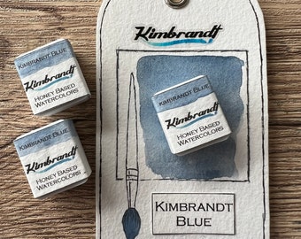 May include: Three small watercolor paint pans labeled "Kimbrandt Blue" with the text "Honey Based Watercolors". A larger label with the text "Kimbrandt Blue" and a drawing of a paintbrush.