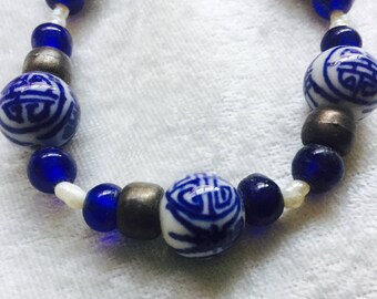 May include: A blue and white porcelain bead necklace with silver accents. The beads feature a repeating Chinese character design.