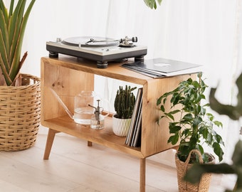 Könnte beinhalten: Ein Holzständer für einen Plattenspieler mit einem Plattenspieler, Schallplatten, Pflanzen und einer Gießkanne. Der Ständer hat eine helle Holzoptik und ist mit Pflanzen und anderen Gegenständen dekoriert.