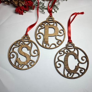 May include: Three wooden Christmas ornaments with red ribbon hangers. Each ornament is a circle with a decorative swirl design and a letter in the center: S, P, and C.