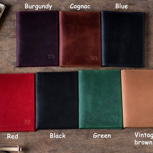 May include: Eight leather passport covers in different colors: burgundy, cognac, blue, red, black, green, vintage brown. Each cover has a different letter monogram.