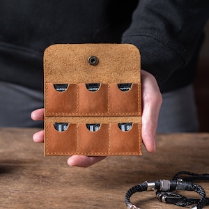 May include: A brown leather case with eight slots for memory cards. The case is open and the slots are empty.