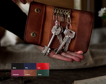 May include: A brown leather key holder with a metal key ring and multiple keys. The key holder is being held in a hand.